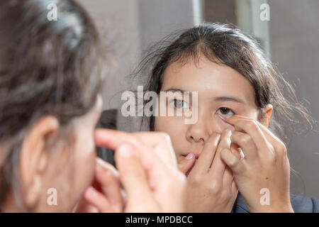 Giovani teenage schoolgirl utilizza uno specchio per rimuovere il suo lenti a contatto Foto Stock