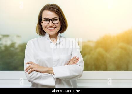 Ritratto sorridente donna medico medico in ospedale con una finestra in background Foto Stock