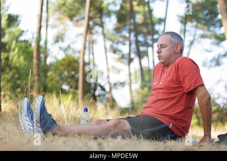 Uomo di mezza età seduto sul terreno mentre fuori esercizio Foto Stock