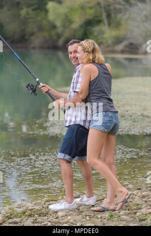 Coppia giovane angling permanente sulla riva del fiume Foto Stock