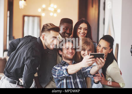 Multirazziale persone divertirsi presso il cafe prendendo un selfie con il telefono cellulare. Un gruppo di giovani amici seduti al ristorante tenendo autoritratto con smart phone
