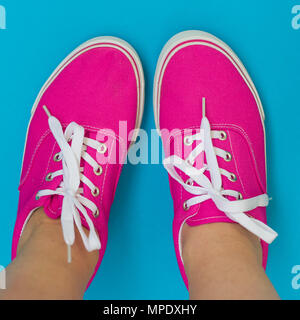 Gambe in rosa sneakers su uno sfondo blu Foto Stock