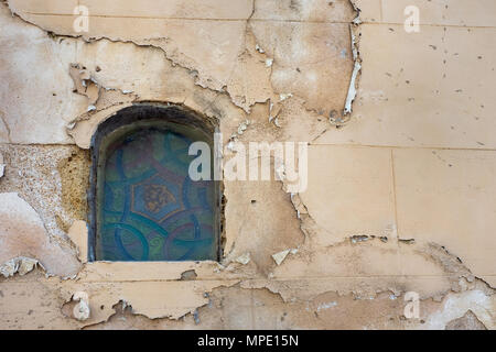 Piccola finestra ad arco con un vintage vetro colorato sul vecchio muro della casa con crepe e macchie di acqua sulla superficie. Foto Stock