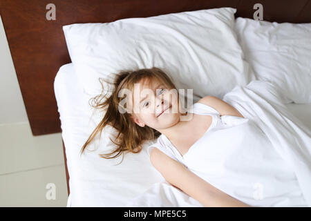 Bambina che giace nel letto e sorridente in mattina. Foto Stock