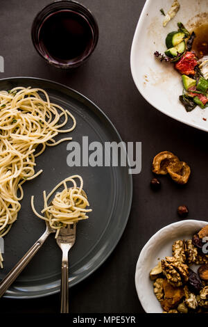 Pasto incompiuto di spaghetti con insalata, dadi e bevande su una superficie di colore grigio. Foto Stock