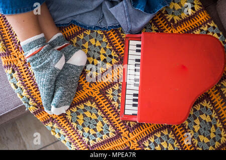 Donna piedi rilassante con belle calze a casa in posizione di riposo. piccolo pianoforte giocattolo sul divano vicino a lei. Musica e vita dell'artista di pattern con coperchio con vint Foto Stock