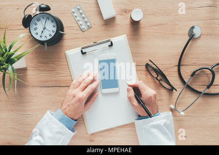 Vista aerea del medico maschio scrivere le note mediche del paziente o di storia della medicina prescrizione sulla carta per appunti durante esame medico in ospedale offi Foto Stock