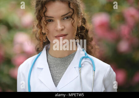 Ritratto di una giovane donna, medico, professionista sanitario, medico, medico indossando un camice in naturale all'aperto con impostazioni blosso Foto Stock