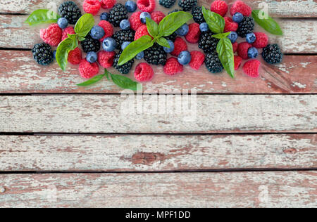 Varie estate freschi frutti di bosco su sfondo di legno. Mature lamponi, more, mirtilli e le foglie di basilico. Frutti di bosco al confine di immagine con copia Foto Stock