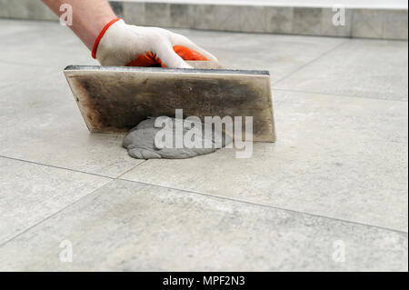 Sigillatura delle fughe di piastrelle ceramiche. Piastrellista riempiendo lo spazio tra le piastrelle con una spatola di gomma. Foto Stock