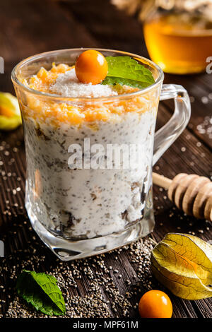 Yogurt probiotici con semi di Chia, noce di cocco, miele e physalis purea in un vasetto di vetro Foto Stock