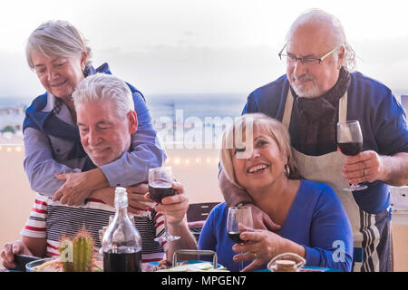 Seniors caucasica adulto soggiorno insieme all'aperto facendo il pranzo in terrazza. vacanza e concetto di amicizia con sorrisi e il vino e il tempo del partito Foto Stock