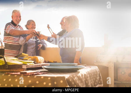 Gruppo di alti persone che fanno parte e un barbeque all'aperto sulla terrazza del tetto. celebrazione e tempo di evento al tramonto. di felicità e di bello stile di vita Foto Stock