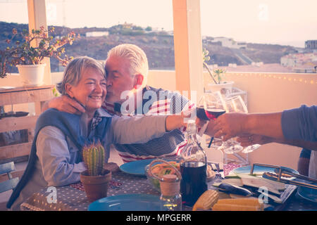 Il gruppo di età compresa tra i senior amici adulti aventi la cena e facendo parte bel tempo in terrazza all'aperto con vino e cibo. divertendosi e kiss du Foto Stock