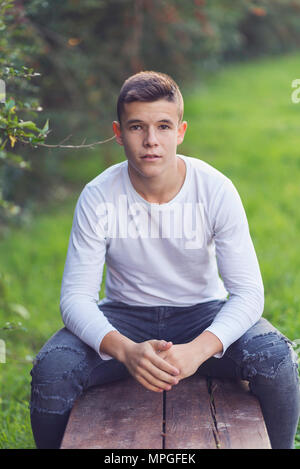 Elegante ragazzo seduto su una panca in legno su un parco cittadino Foto Stock