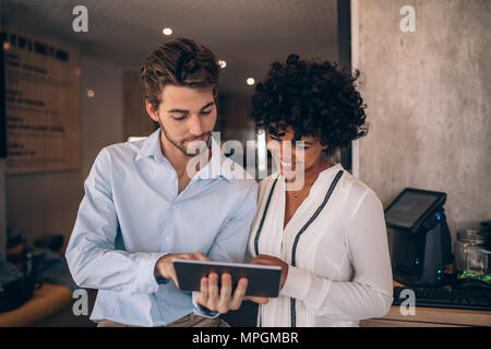 Due ristorante business partner in piedi insieme e guardando a tavoletta digitale. L uomo e la donna con tavoletta digitale in una caffetteria. Foto Stock