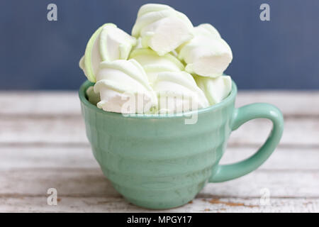 La menta piperita grande marshmallows in una grande tazza verde su sfondo blu Foto Stock