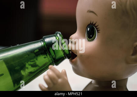 Faccia di una bambola di plastica a bere birra in una bottiglia di vetro, il concetto di immagine Foto Stock