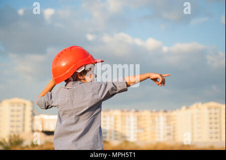 Ragazzo in arancione casco punti con il suo dito in direzione piedi su sfondo di nuovo costruito case Foto Stock