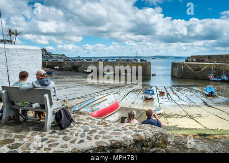 Vacanzieri relax sui posti a sedere con vista porto Mousehole in Cornovaglia. Foto Stock