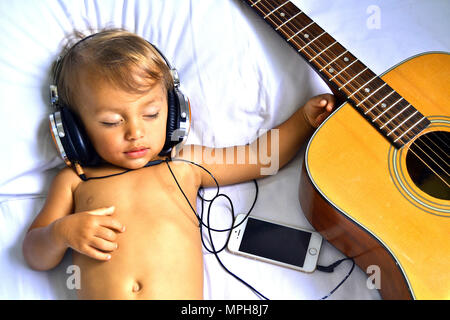 Bambino addormentato con le cuffie accanto alla chitarra Foto Stock