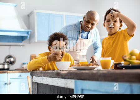 Caring giovane padre guardando i suoi figli a mangiare la prima colazione Foto Stock