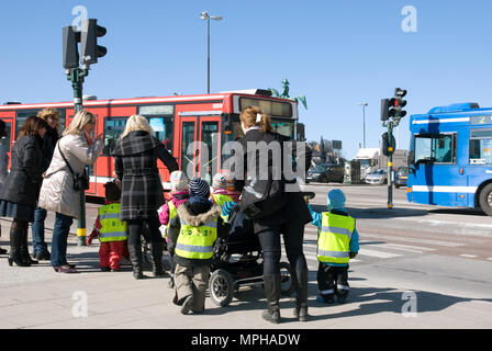 Stoccolma, Svezia - 14 Aprile 2010: gli educatori con kindergarten i bambini vestiti in giubbotti di sicurezza e giubbotti riflettenti da su crosswalk in centere di Stoccolma Foto Stock