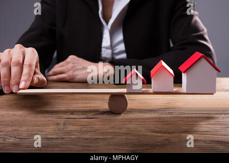Close-up di un dito umano equilibratura di modelli della casa su altalena sulla scrivania in legno Foto Stock