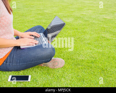 Piuttosto giovane donna utilizzando computer portatili. Lavoro femminile sul computer portatile in un esterno di erba verde campo Foto Stock