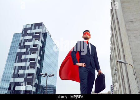 Un imprenditore in un costume da supereroe si erge contro un business b Foto Stock