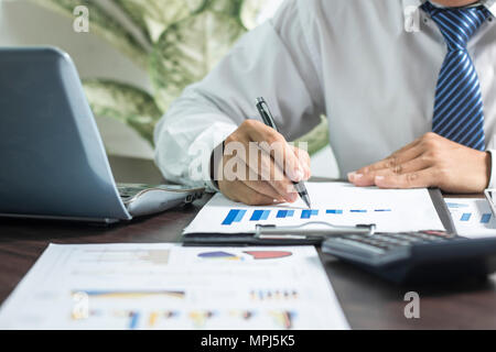 Imprenditore il controllo sulla carta delle finanze dopo aver premuto sulla calcolatrice, analisi e pianificazione il profitto della società su un foglio di carta millimetrata sul tavolo di lavoro Foto Stock