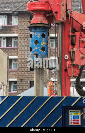 Un enorme di foratura o di palificate rig in uso su un cantiere nel centro di Londra con un operaio in indumenti ad elevata visibilità sul sito. Driver di pelo. Foto Stock