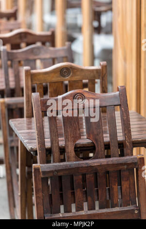 Alcuni tavoli in legno e sedie in righe come posti a sedere davanti a o al di fuori del bar o ristorante per diners per mangiare fuori di porte. arredamento tradizionale. Foto Stock