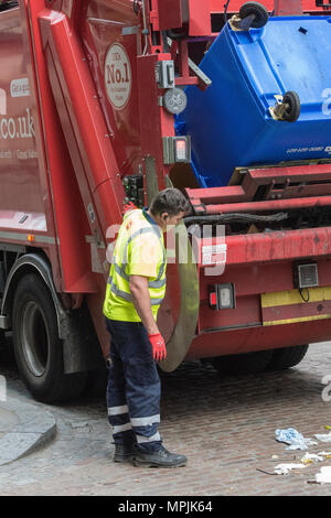 Un uomo il funzionamento di un meccanismo di dustcart o bin raccolta con un autocarro. Gli uomini lo scomparto di raccolta scarti e lo svuotamento di rifiutare o bidoni sul giorno di raccolta. Foto Stock