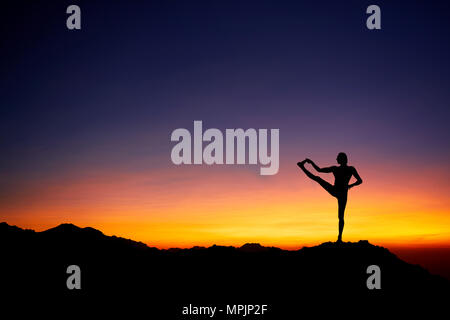 Montare l'uomo in silhouette fare yoga equilibrio pongono in corrispondenza di un bel colore arancione tramonto sullo sfondo del cielo Foto Stock
