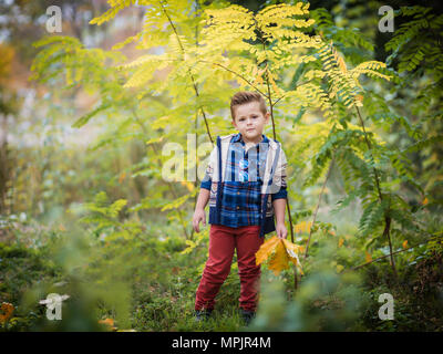 Little Boy giocando in giallo fogliame. Autunno nel parco della città. Foto Stock