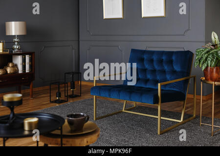 Foto reale di un grande, blu navy poltrona con cornice dorata contro la parete scura con lo stampaggio in elegante salone interno Foto Stock