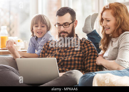 La famiglia felice di guardare un film insieme. Uomo con notebook tra figlio sorridente e moglie Foto Stock