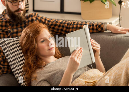 I capelli rossi donna la lettura di un libro e il marito seduto dietro di lei Foto Stock