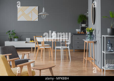 Sedie bianche al tavolo da pranzo in grigio interno dell appartamento con dipinto di giallo e poltroncina in legno Foto Stock