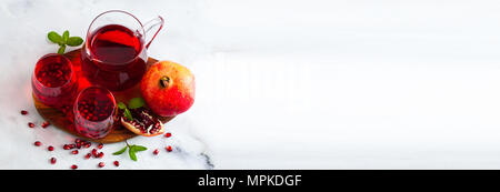 Preparate di fresco il succo di melograno in un decanter e due bicchieri su una tavola di marmo e una pietra grigio Sfondo con foglie di menta e semi di frutta Foto Stock