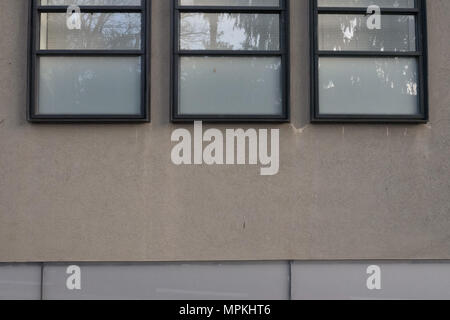 Tre finestre in metallo fotogrammi neri sulla parete, il vetro riflette il cielo grigio. Foto Stock