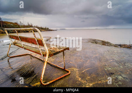 Rusty banco da parte del mare a Helsinki in Finlandia, su una molla giorno nuvoloso Foto Stock