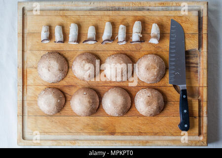 Funghi champignon caps e piccioli sul tagliere di legno in ordine con il coltello da sopra Foto Stock