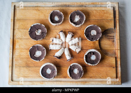 Funghi champignon caps capovolto e piccioli sul tagliere di legno disposte in cerchio con dal di sopra Foto Stock
