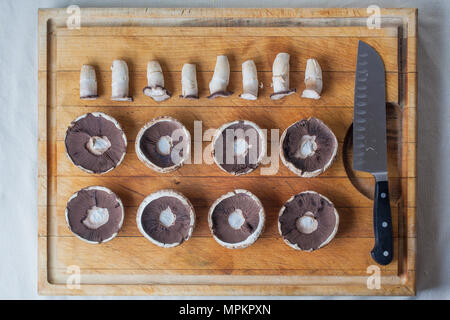 Funghi champignon è capovolto i cappucci e piccioli sul tagliere di legno in ordine con il coltello da sopra Foto Stock