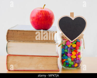 Giornata Mondiale del Libro concetto. Red apple ha messo sulla pila di libri vecchi con cuore nero e colorato di stons in vaso Foto Stock