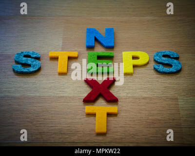 Prossimi passi concetto in lettere colorate sulla lavagna in legno Foto Stock