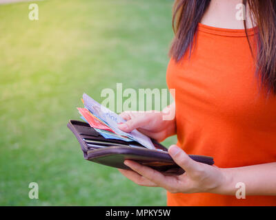 Le donne le mani tenendo fuori i soldi della Malaysia ringgit dal portafoglio sul verde del campo di erba Foto Stock