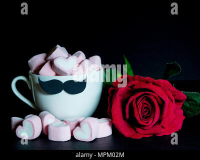 La festa del papà concetto. Con una rosa rossa e dolce marshmallow a forma di cuore in una tazza da tè con baffi neri su sfondo scuro Foto Stock